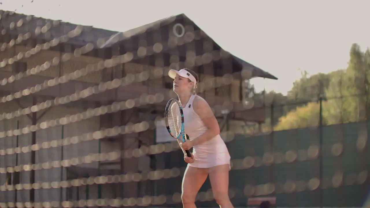 A professional woman in a white tight suit hits the ball with a racket and dynamically plays on the tennis court