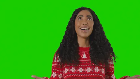 Studio Portrait Of Woman Wearing Christmas Jumper Against Green Screen With Hands Out To Catch Falling Snow