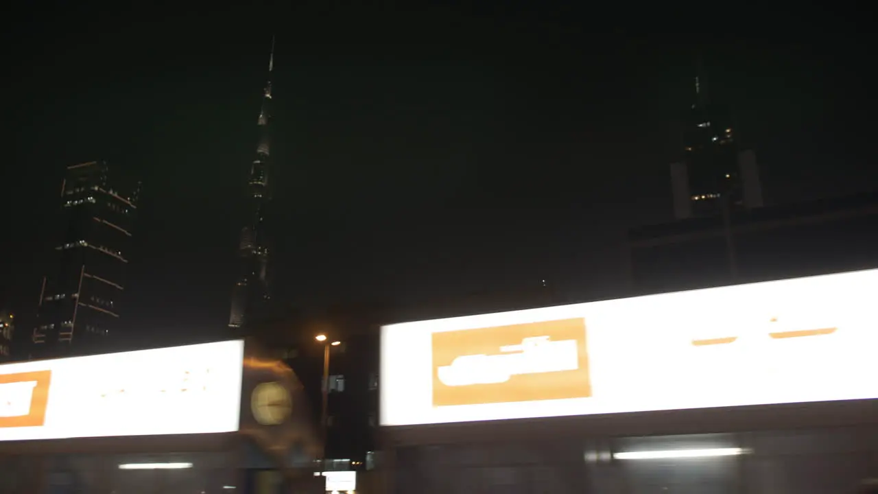 Passing by Dubai skyline at night time in a car on the highway with distant lit up buildings and skyscrapers including the Burj Khalifa in the United Arab Emirates