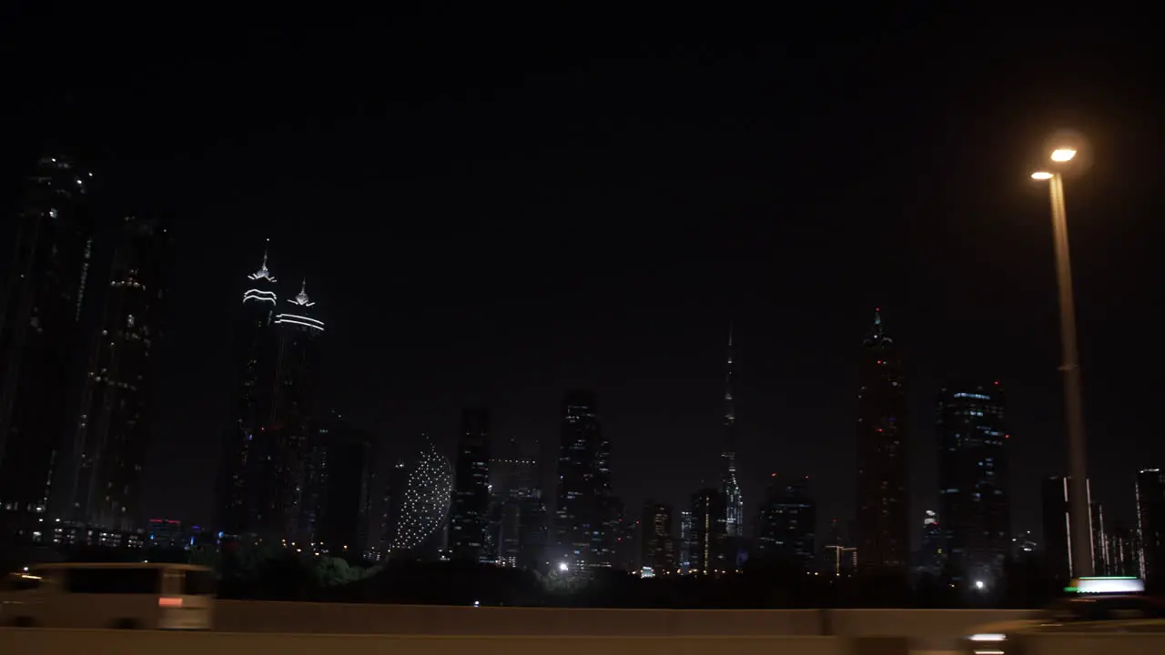 Passing by the Dubai skyline at night in a car on the highway with distant lit up buildings and skyscrapers including the Burj Khalifa in the United Arab Emirates