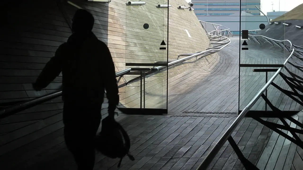 The silhouette of a man with a backpack in his hands enters through the automatic glass door of International Port Terminal of Yokohama Japan