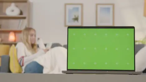 Woman Relaxing On Sofa Using Mobile Phone At Home With Green Screen Laptop In Foreground 