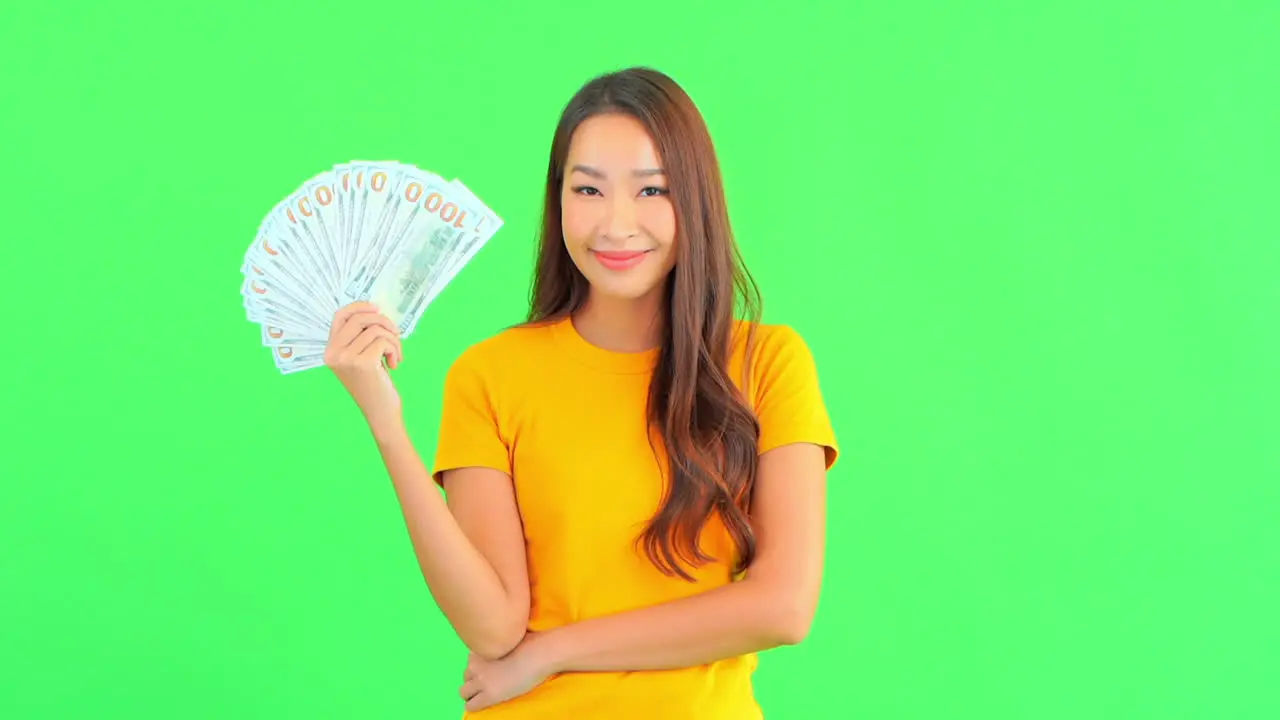 Young lady holding a paper bills in her hand and pointing at it with a smile on her face and positive energy isolated on a green screen