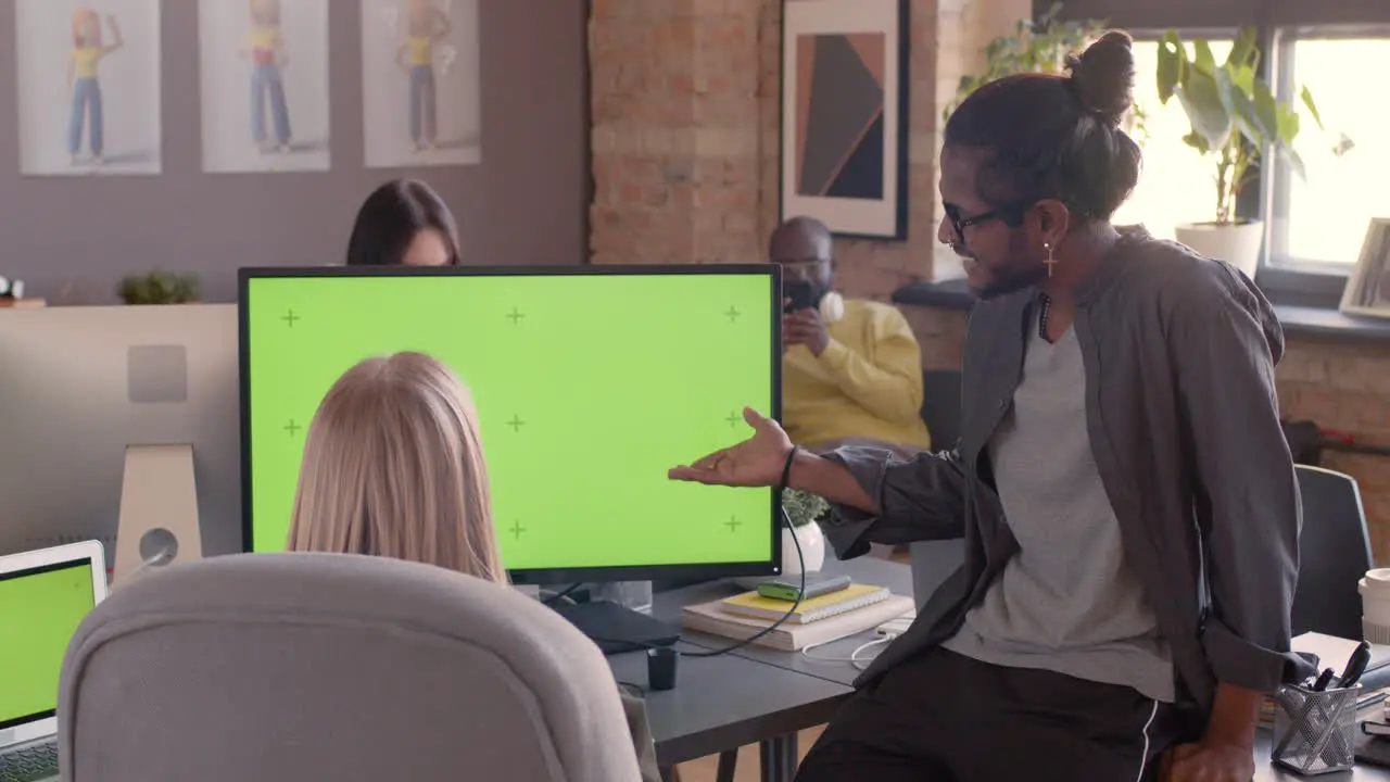 Two Multiethnic Colleagues Looking At Monitor With Green Screen And Discussing New Project In An Animation Studio