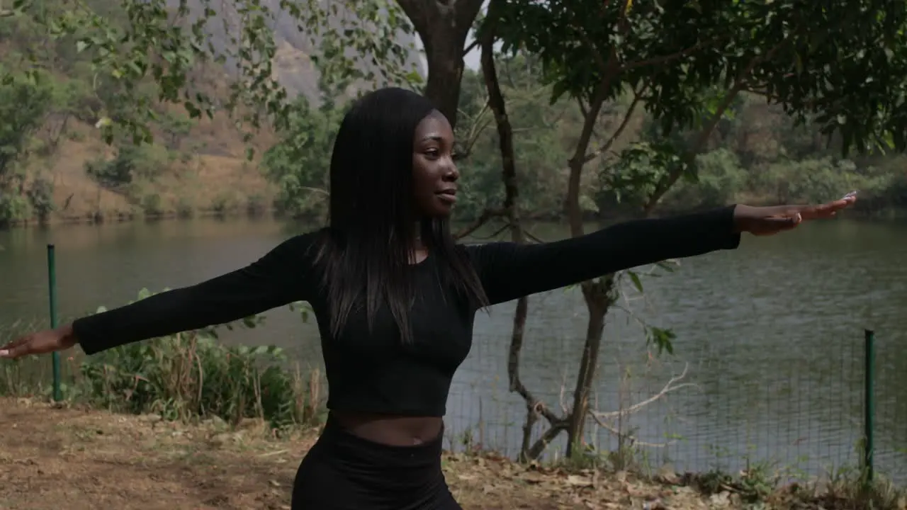 Medium shot of a girl stretching in a warrior pose by the lake