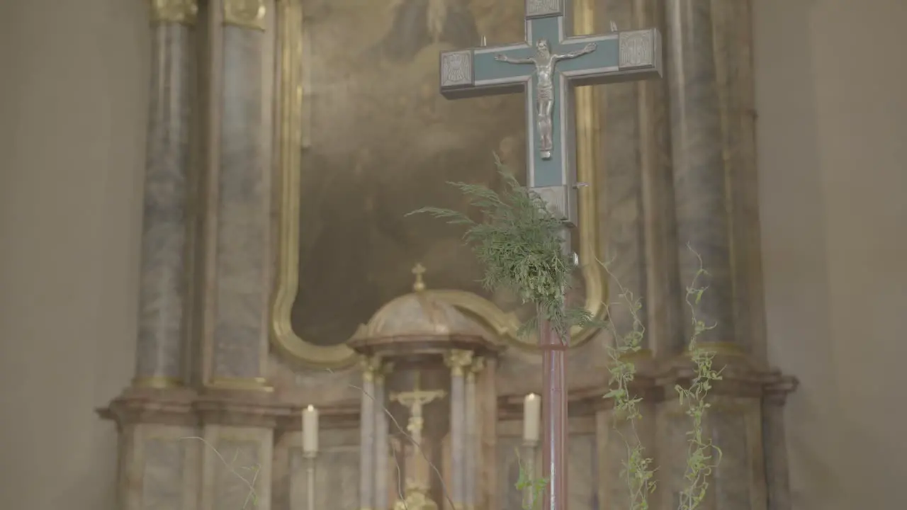 Camera pans to a cross in the sanctuary of a church with a baroque altar in the background