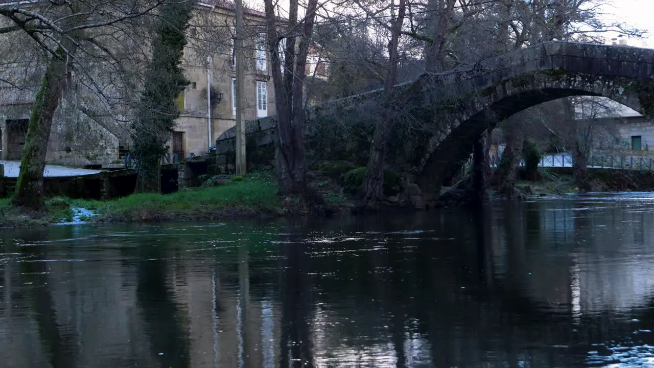 Reflection of Banos de Molgas city in river with Roman bridge