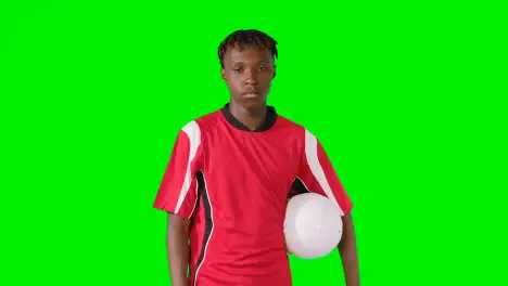 Studio Portrait Of Male Footballer Wearing Club Kit With Ball Under Arm Against Green Screen