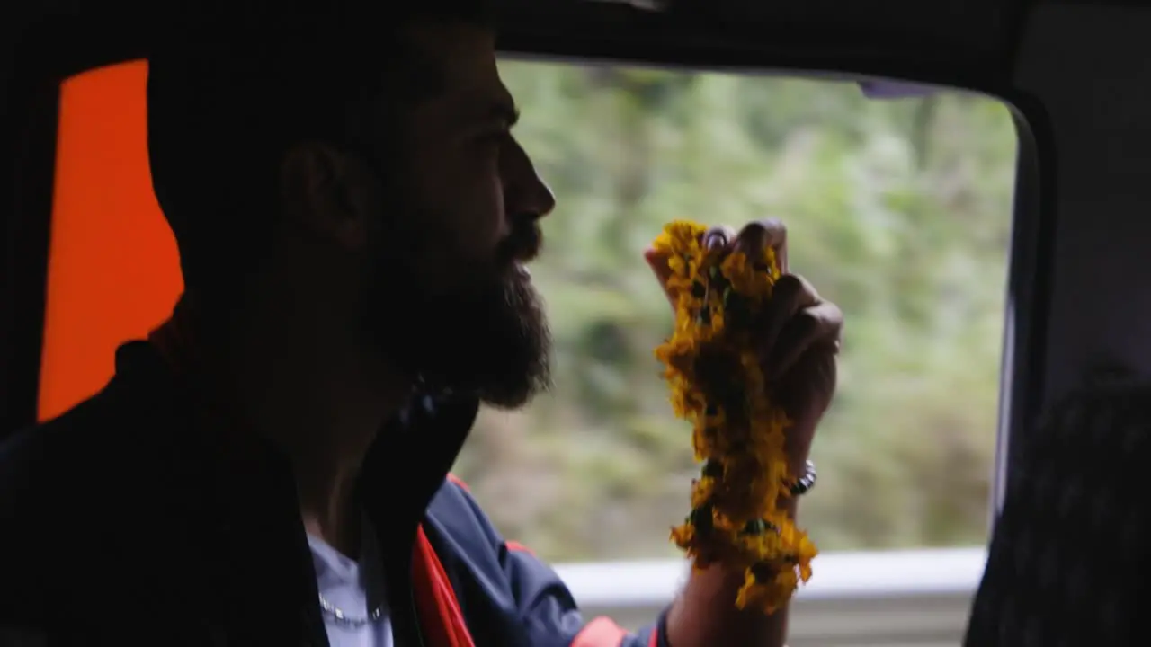 Man with full beard holding yellow prayer flowers stairs dramatically out window of car