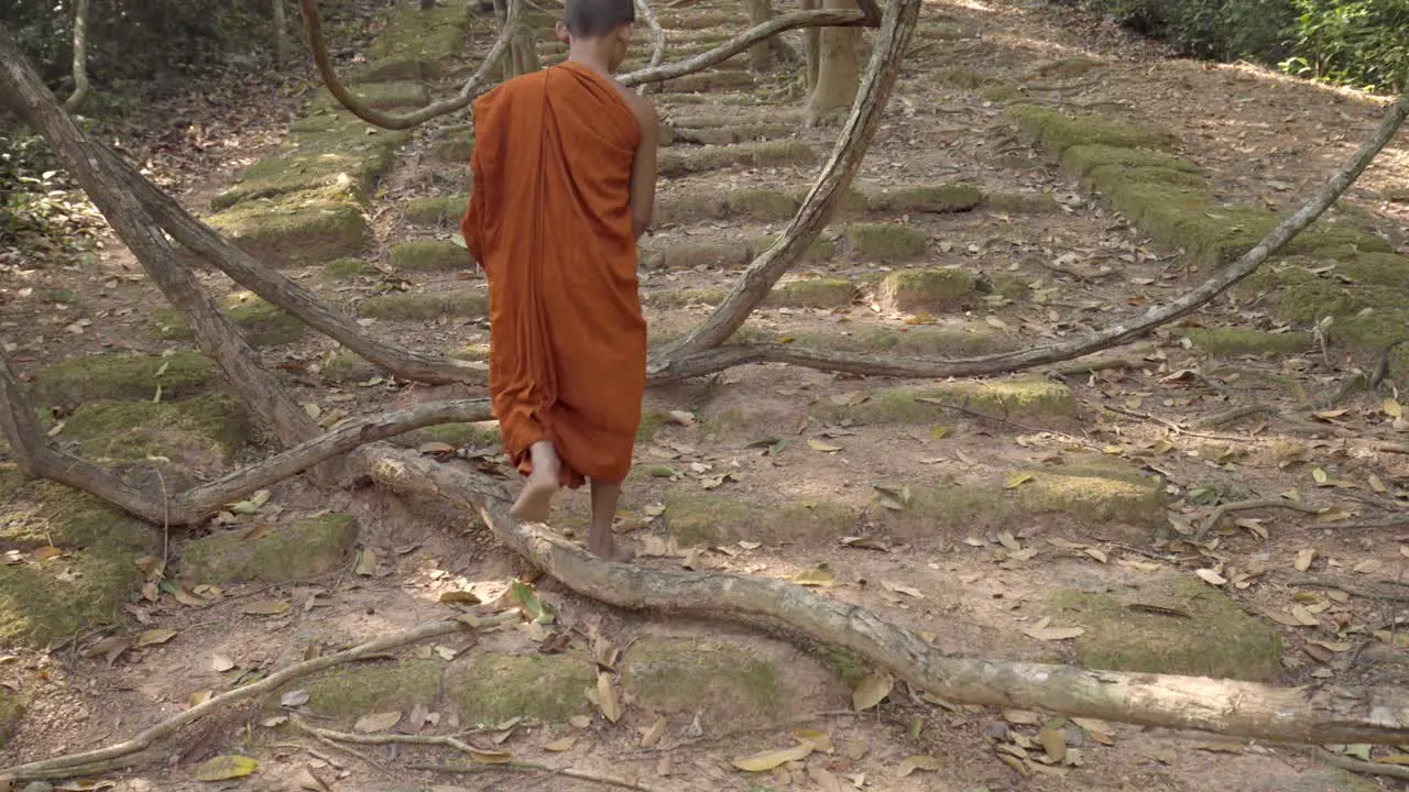 Bare footed Monk in saffron robes walking over remote Angkorian sandstone rocky pathway through the jungle