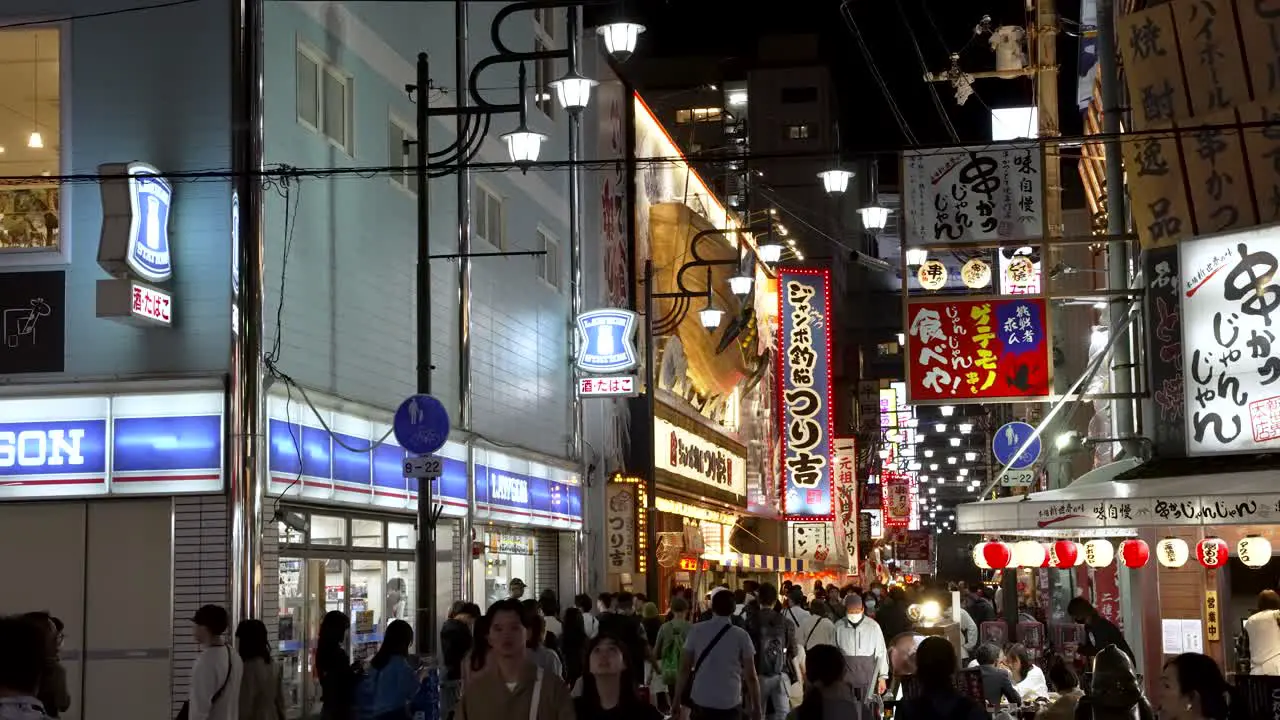 Crowds Of People Walking Through Shinsekai Area At Night Past Lawsons Store