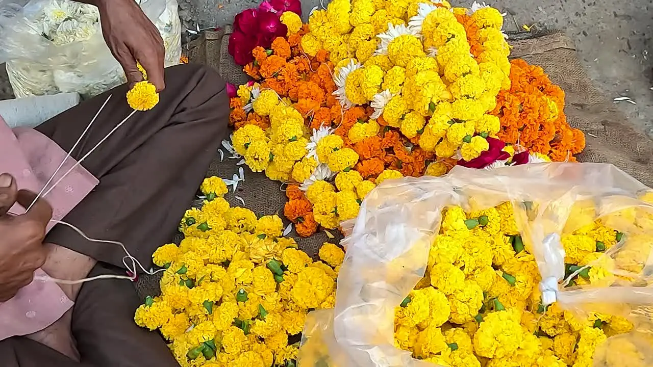 A shopkeeper is making fresh flower garlands on Street Road