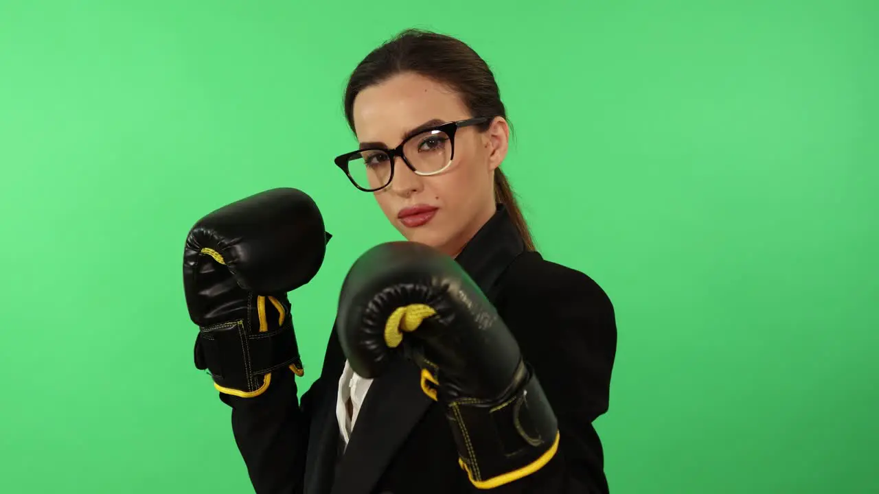 Businesswoman with glasses and ponytail wearing white shirt and black business attire uses boxing gloves to punch toward camera