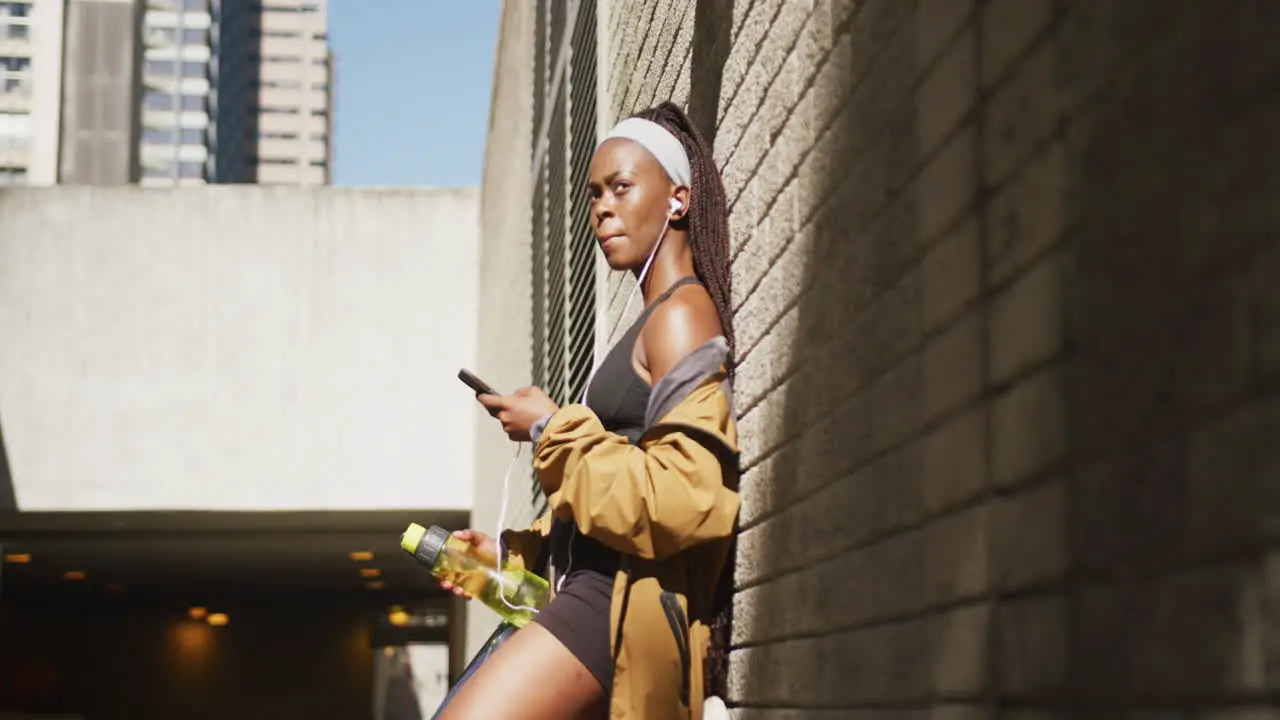 African american woman exercising outdoors wearing earphones using smartphone in the city