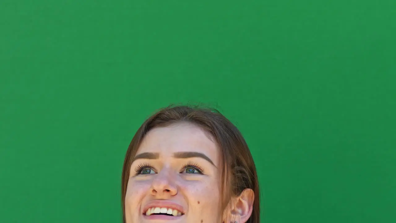 Close up smiling girl's head against green screen looking up and around