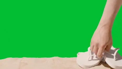 Summer Holiday Concept Of Hand Picking Up Flip Flops Beach Towel On Sand Against Green Screen 1