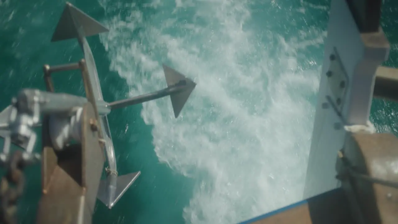 Mid shot of rear end of boat cruising across the ocean with anchor in foreground