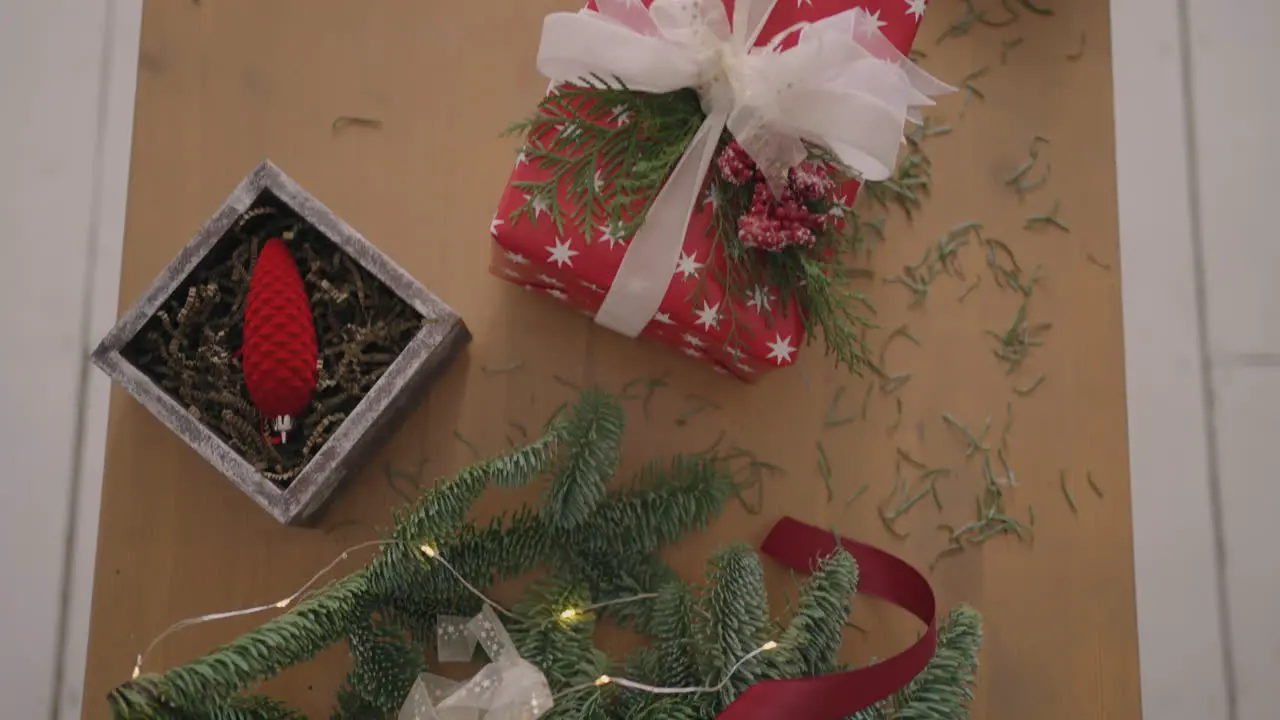 top view plan Fully visible the table with the decorations Female hands put and finalize Christmas gift wrapped in craftool paper on a wooden table Bandaging tape and tied bow