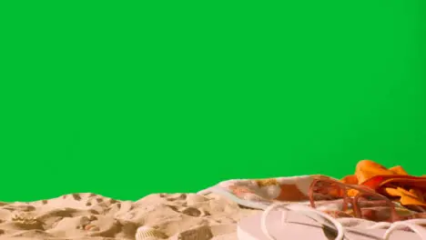 Summer Holiday Concept Of Sunglasses Swimsuit Flip Flops Beach Towel On Sand Against Green Screen