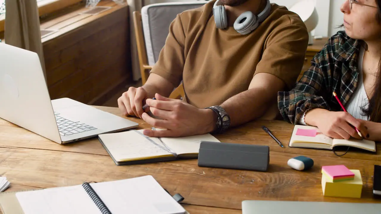 Camera Focuses On A Student With Headphones Talking With Female Mate Using Laptop Then Focuses Items Over The Table