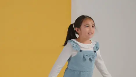 Studio Portrait Of Hyperactive Girl Smiling And Jumping Against Yellow And White Background