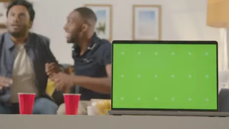 Two Men Celebrating Watching Sports Game On TV At Home With Green Screen Laptop In Foreground 1