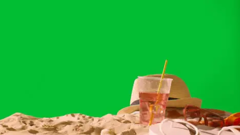 Summer Holiday Concept Of Cold Drink On Beach Towel With Flip Flops Sunglasses And Sun Hat Against Green Screen