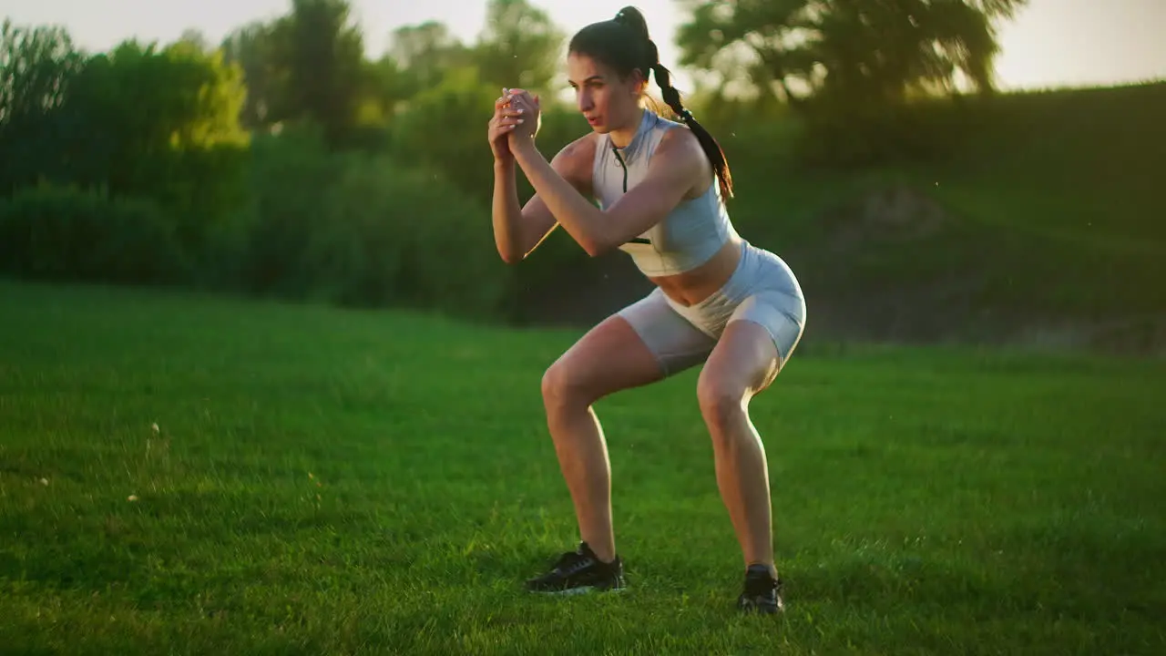 A young woman jumps a burpee exercise in a Park on the grass at sunset Slow motion fitness training of a young woman in a meadow