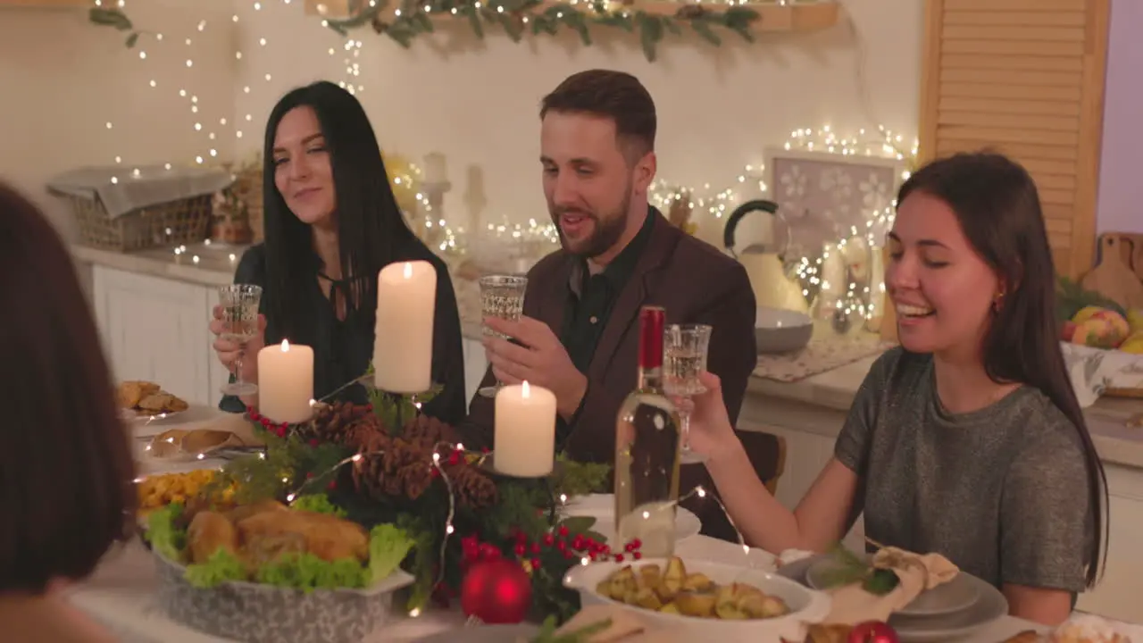 Group Of Happy Friends Sitting At Table Holding Champagne Glasses And Talking To Each Other At Home On Christmas 1