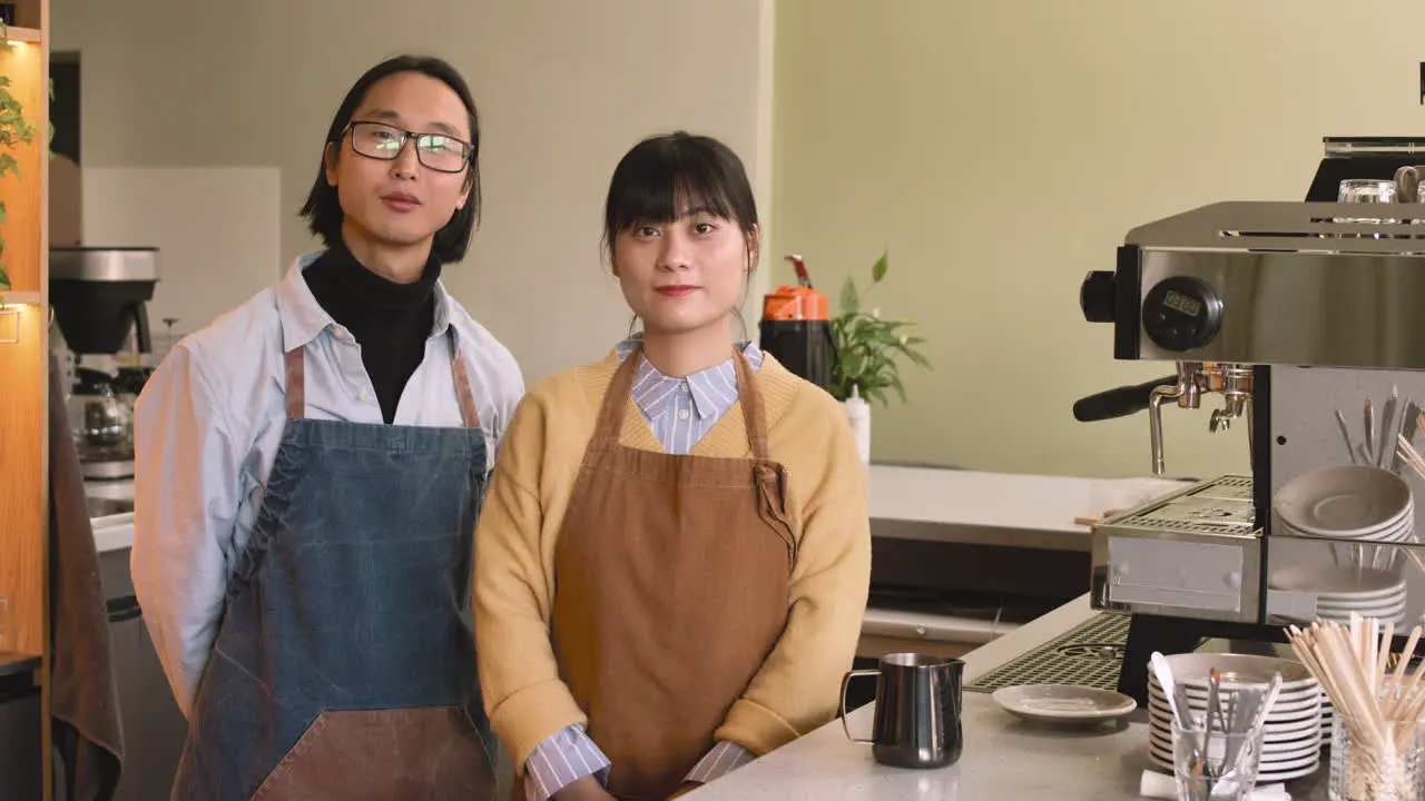 Two Waiters Smiling At Camera While Standing Behind Counter In A Coffee Shop