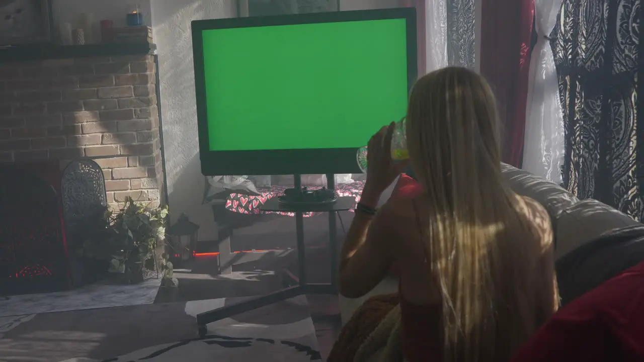 Green screen television on misty hazy morning with blonde women lady girl sitting on couch cuddled up with blanket watching and drinking from wine champagne water glass and checking her phone