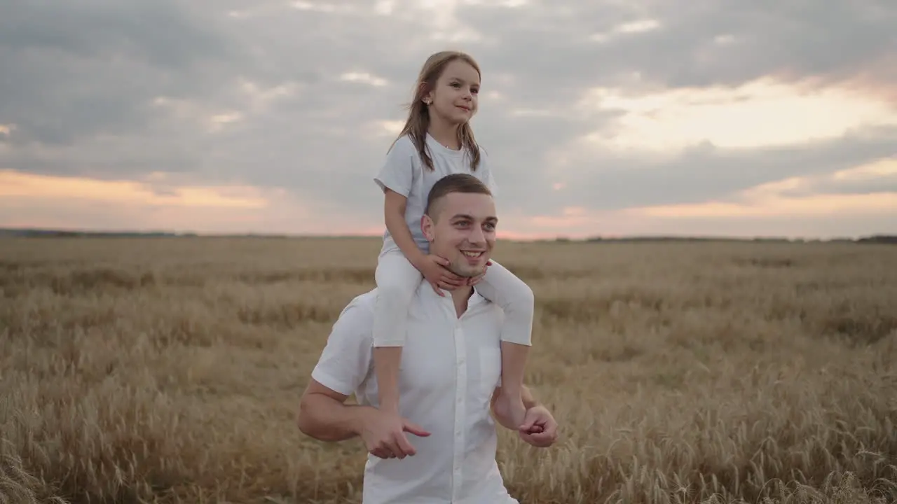 happy child and father are playing in field of ripening wheat little daughter on fathers shoulders baby boy and dad travel on field kid and parent play in nature happy family and childhood concept