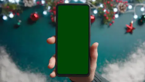 Overhead Shot Of Person Holding Green Screen Mobile Phone Above Christmas Decorations 2