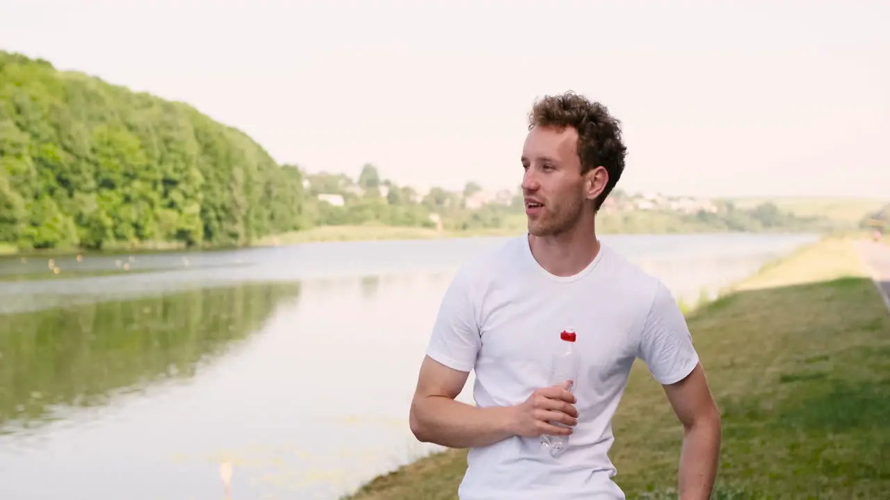 Fitness Junger Mann Ruht Und Trinkt Wasser Während Er Sich Nach Dem Lauftraining An Metallgeländern In Einem Park In Der Nähe Des Flusses Lehnt