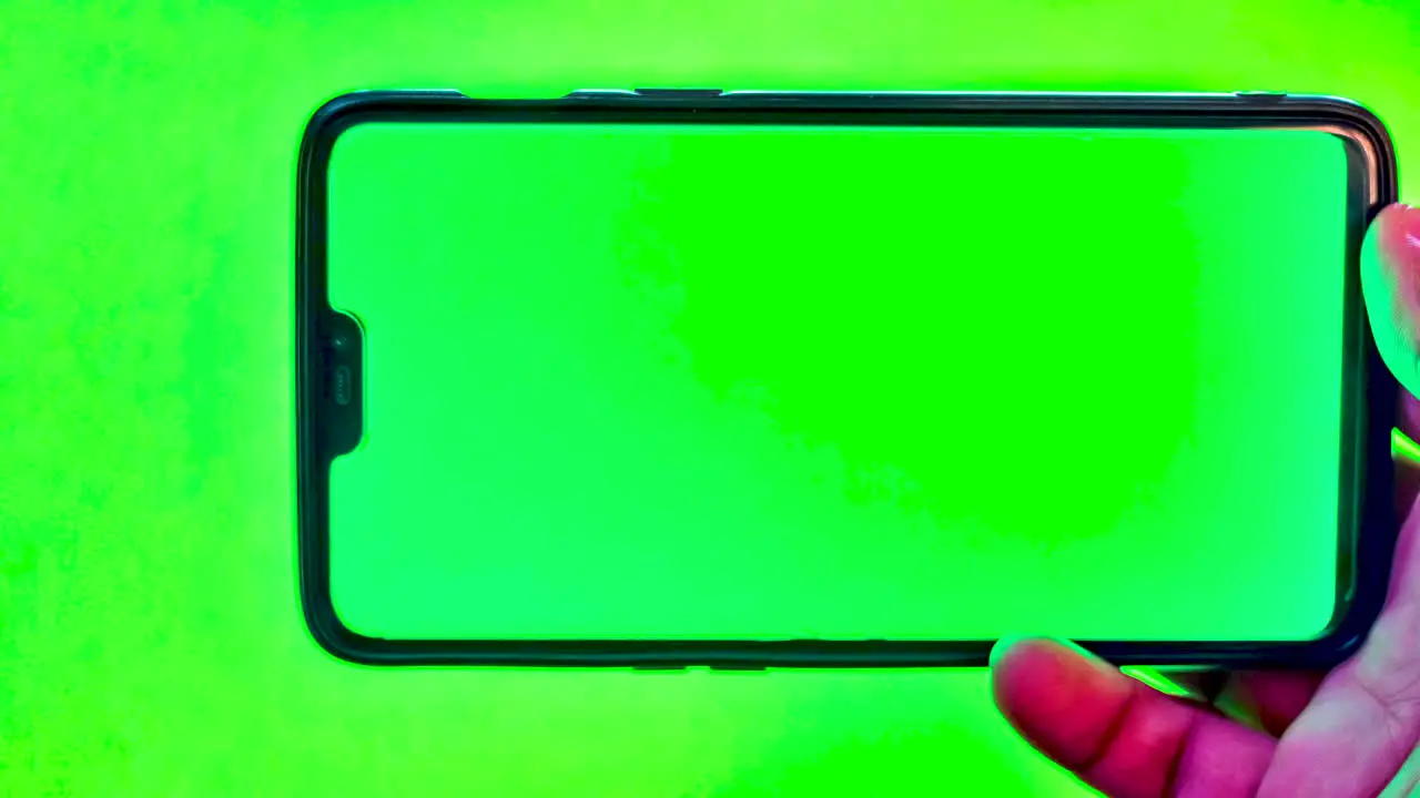 Close-up Hand of an Asian man holding a modern smartphone against green screen background with green display