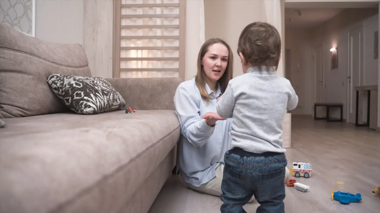 Baby Unternimmt Seine Ersten Schritte In Der Nähe Des Sofas Um Ein Feuerwehrautospielzeug Zu Nehmen Und Es Seiner Mutter Zu Geben