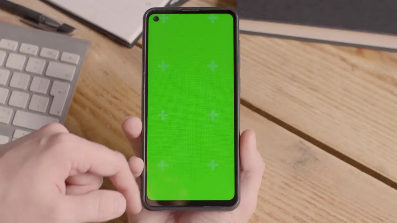 Close Up Of Person Holding Green Screen Mobile Phone On Desk With Hand Scrolling Across Screen 1