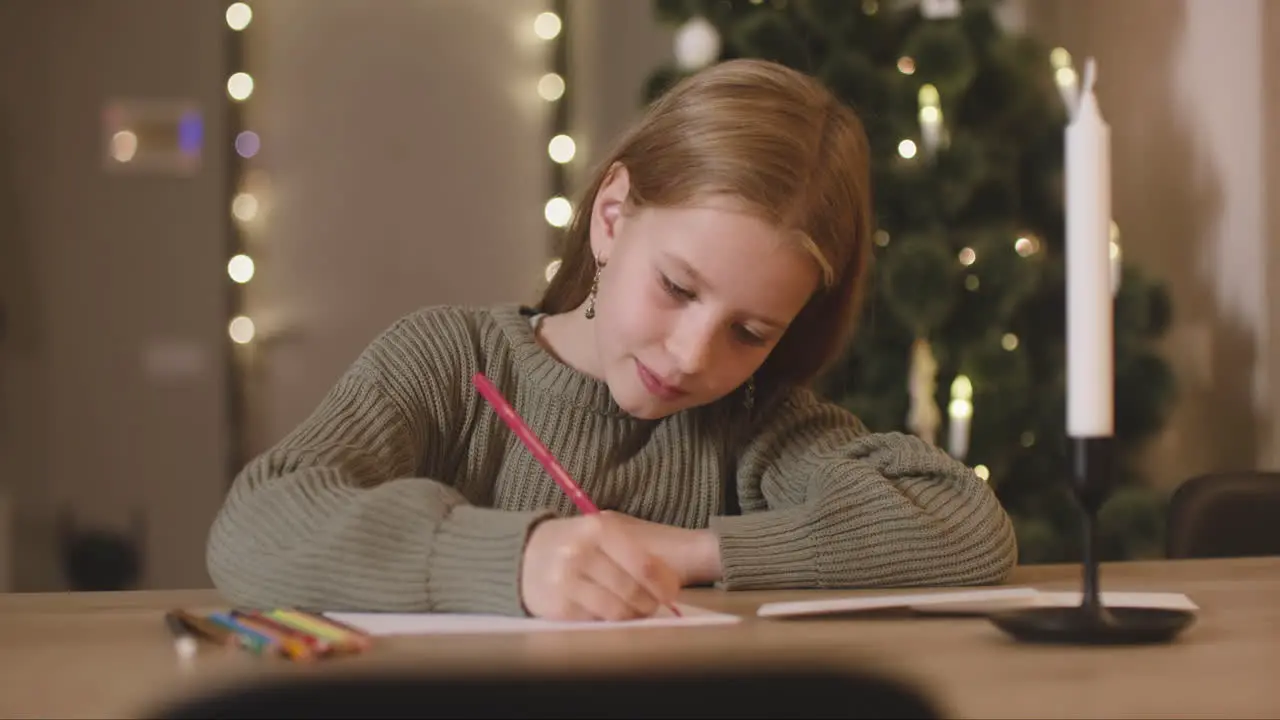 Mädchen In Grünem Pullover Das Einen Wunschbrief Schreibt Sitzt An Einem Tisch In Einem Mit Einem Weihnachtsbaum Geschmückten Raum