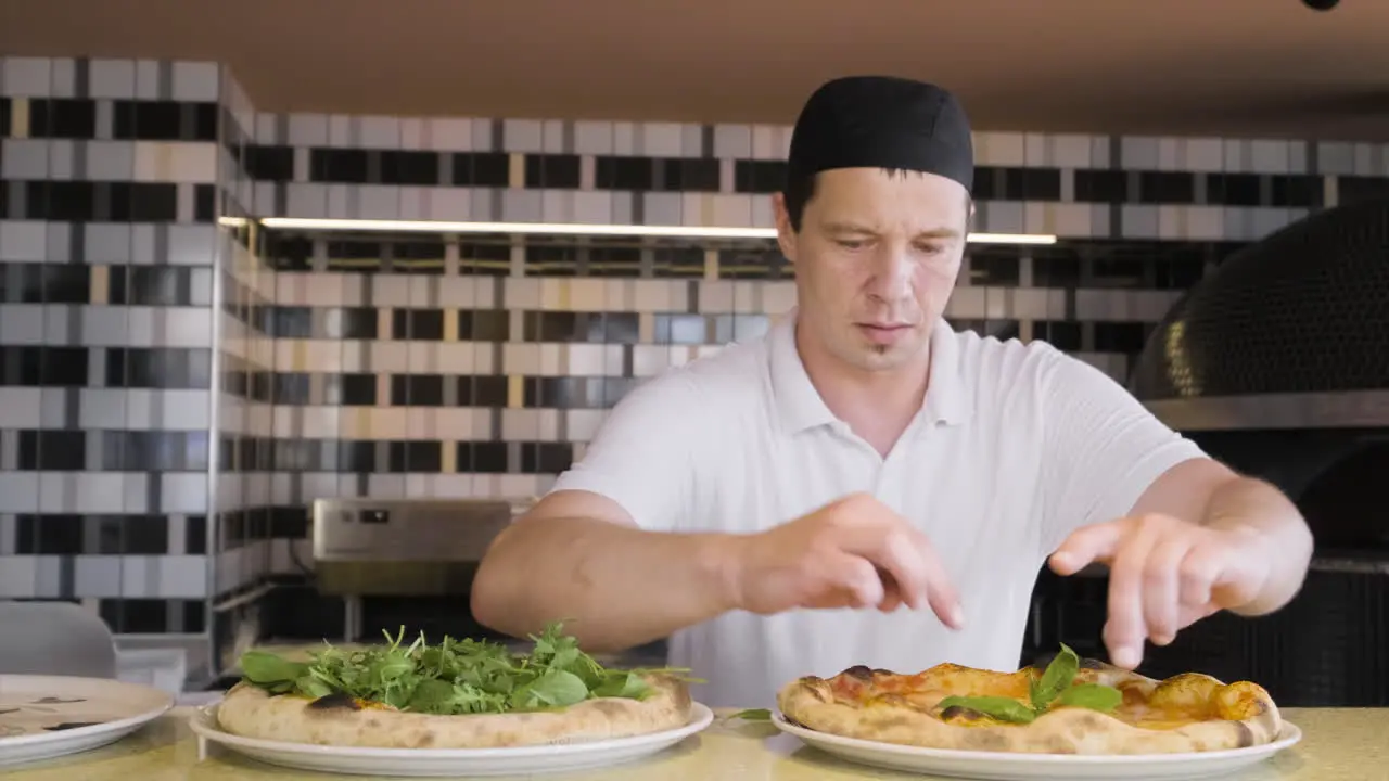 Vorderansicht Eines Kochs Der Basilikumblätter Auf Gebackene Pizzen Legt Und Dann In Die Kamera Schaut