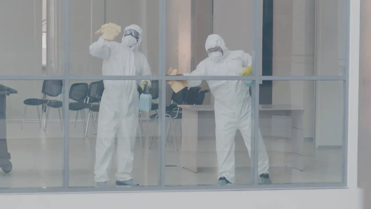 Vista Desde El Exterior De Dos Hombres De Limpieza Que Usan Equipo De Protección Personal Limpiando Cristales Dentro De Un Edificio De Oficinas