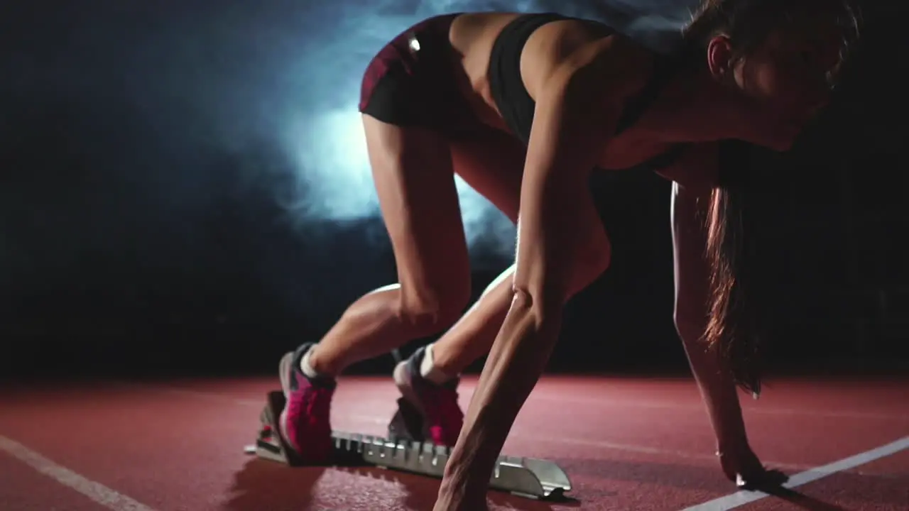 Una Atleta De Fondo Oscuro Se Está Preparando Para Correr El Sprint A Campo Traviesa Desde Las Almohadillas De La Cinta De Correr Sobre Un Fondo Oscuro