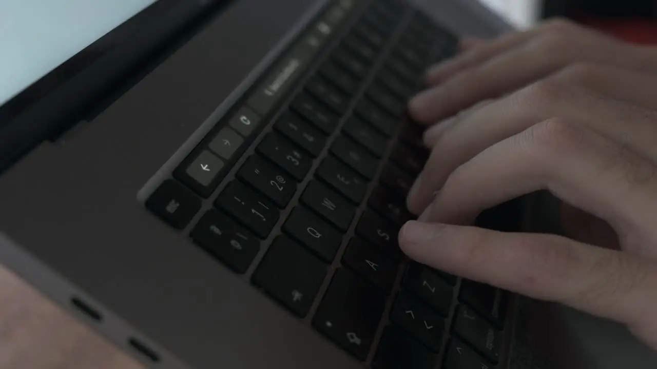 Slow-motion close-up of male fingers typing on grey laptop