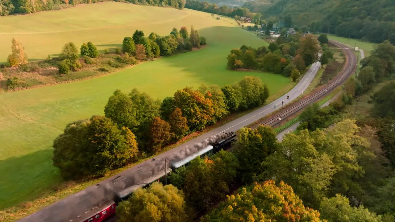 Steam train with passenger cars driving through an autumn landscape on a sunny day