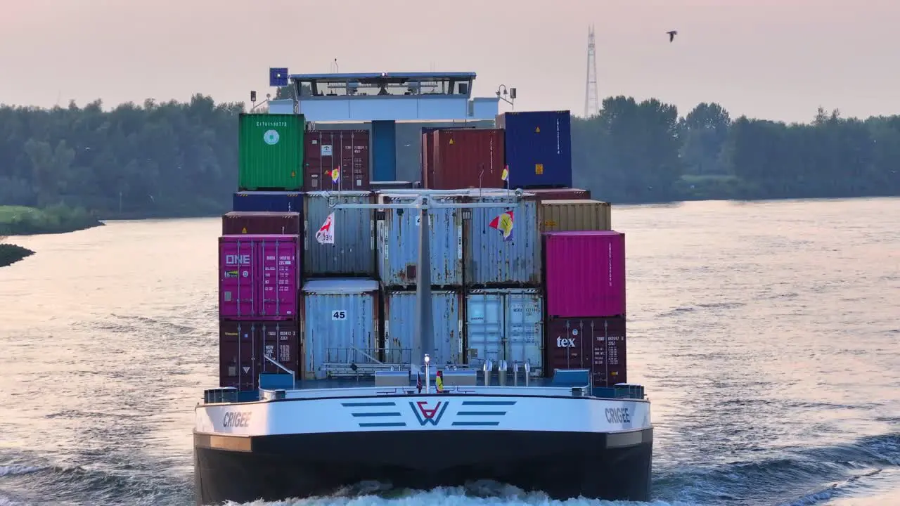 Cargo ship with containers and colored flags Crigee Noord sailing along the banks of the Hoaldn river