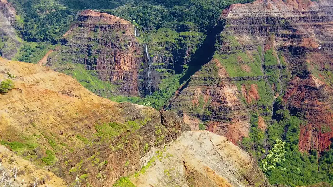 HD Hawaii Kauai slow motion static wide shot of Waimea Canyon with a waterfall in distance and a helicopter entering frame right flying past waterfall