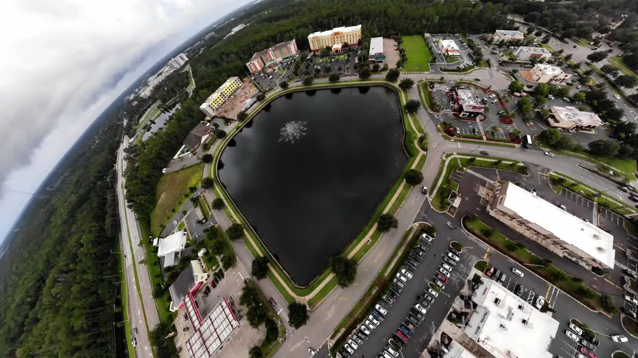 Beautiful aerial zoom out shot of water fountain in pond buildings in background trees in foreground