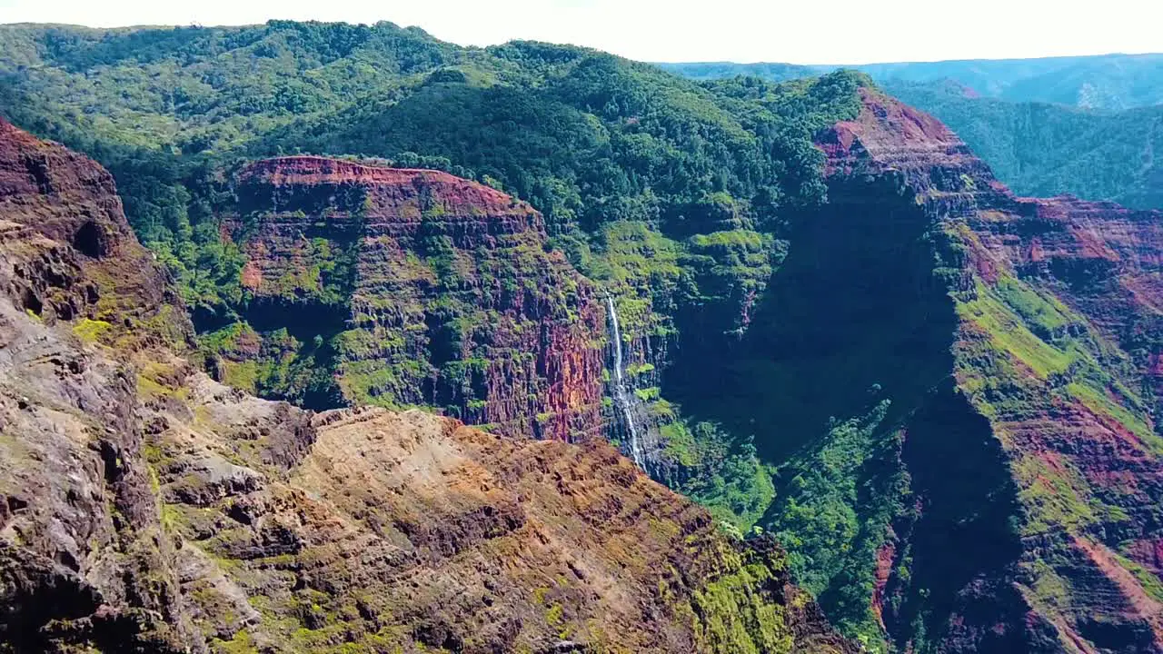 HD Hawaii Kauai slow motion boom down from Waimea Canyon with a waterfall in distance to a tree in foreground right