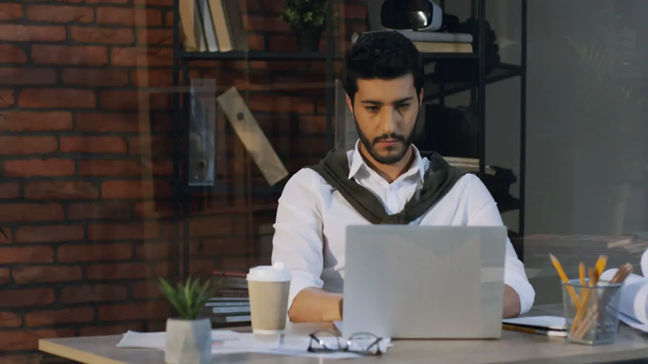 Good Looking Arabian Businessman Sitting At The Table And Working On The Laptop Computer Then Drinks Coffee