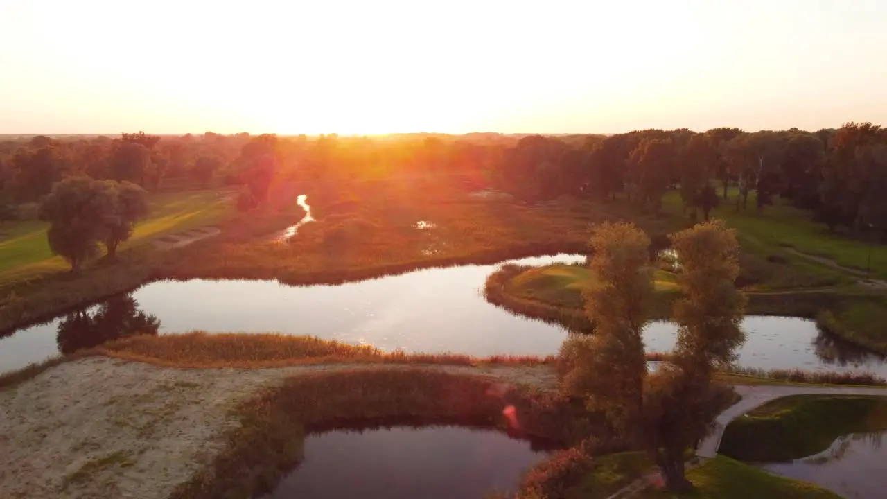 Establishing rising drone shot over golf course during sunny sunset in Warsaw Poland revealing water ponds greens and forest