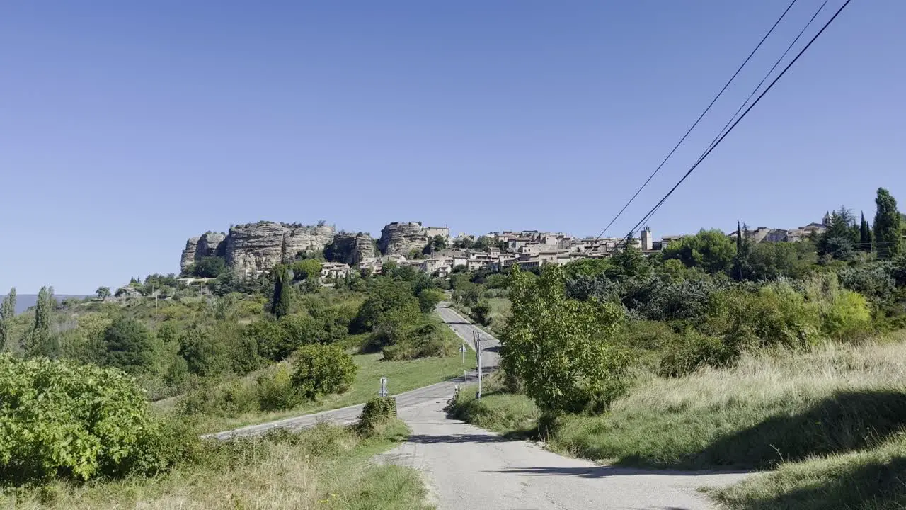 Landscape with a road through nature leading to a small historic stone village in strong sun